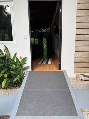 A house entrance with a wooden floor, a grey mat, and a small garden with plants.