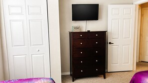 A room with a dark wooden dresser, a flat-screen TV mounted on the wall, and a door with a sign. - Full BR Resort near Disney/Pool, Jacuzzi, Splash, Lake, Club House/& Family Fun (Kissimmee)