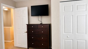 Een kamer met een gesloten witte deur, een donker houten dressoir met lades en een wandgemonteerde flatscreen televisie.