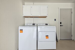 Een wasserette met twee witte voorladers wasmachines en drogers, een witte deur en een witte muur.