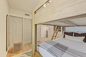 Une chambre avec un lit superposé, une petite échelle, un petit tabouret et une porte donnant sur une autre pièce.