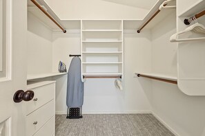Un dressing avec une tringle à vêtements, des étagères et un petit espace dédié au repassage.