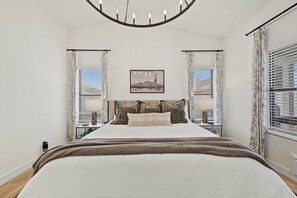 A bedroom with a large bed, two bedside tables, a chandelier, and a window with blinds. - Scottsdale Retreat Private Hot Tub (Scottsdale)