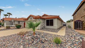 A residential area with houses featuring red-tiled roofs, a central palm tree, and a gravel driveway.