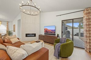 A modern living room with a large flat-screen TV, a fireplace, a green armchair, and a sliding glass door leading to an outdoor area. - Scottsdale Retreat Private Hot Tub (Scottsdale)