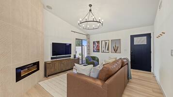 A modern living room with a flat-screen TV, leather sofa, and a chandelier.