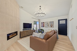 A modern living room with a flat-screen TV, leather sofa, and a chandelier. - Scottsdale Desert Retreat | Private Hot Tub (Scottsdale)