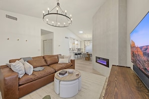 A modern living room with a brown leather sofa, a round wooden coffee table, a flat-screen TV mounted on the wall, and a fireplace. - Scottsdale Retreat Private Hot Tub (Scottsdale)