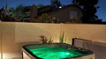 A hot tub with a green light, surrounded by a brick wall, with a house and trees in the background.