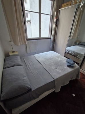A small, single-bed room with a window, a bedside table, and a mirror. - Elegant apartment in La Recoleta. (Buenos Aires)
