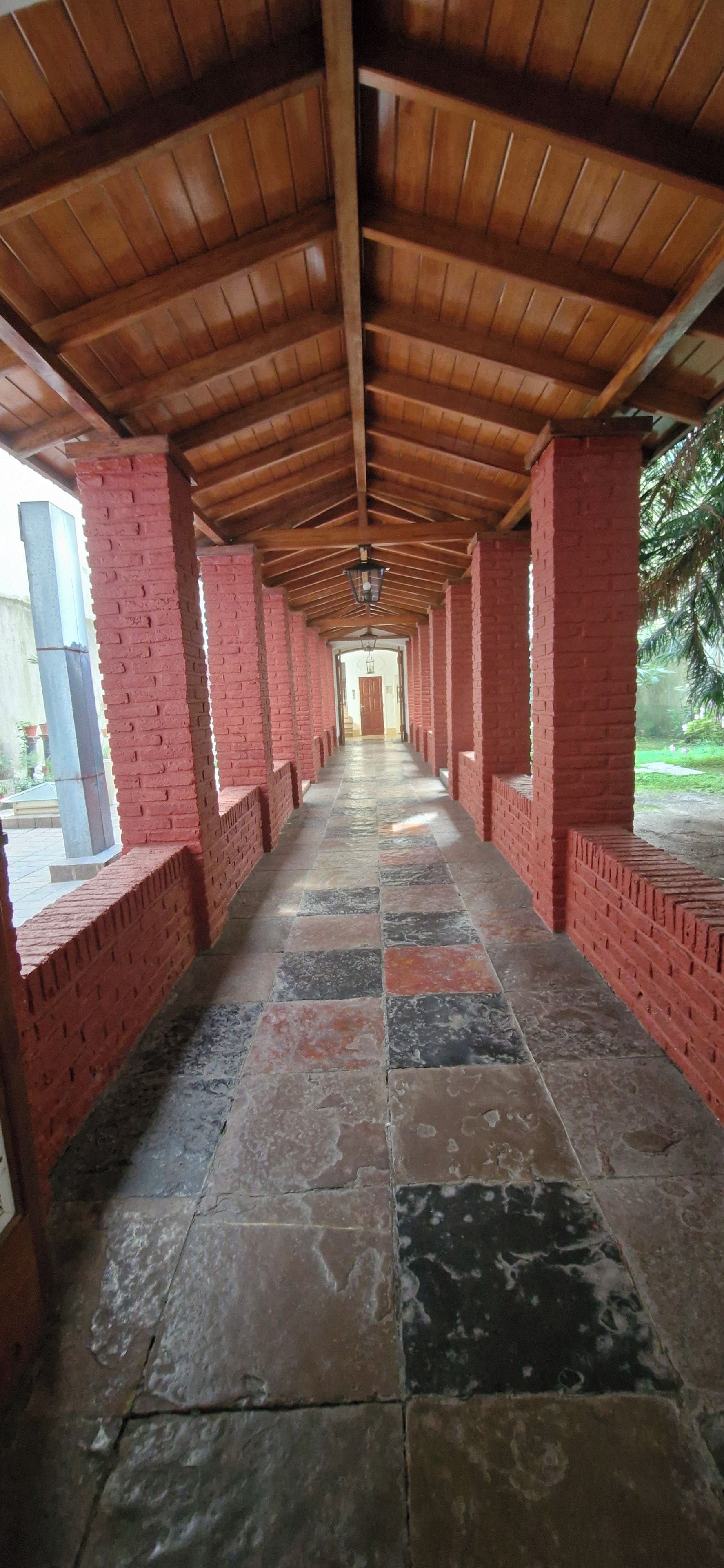 A covered corridor with red brick walls and a tiled floor.