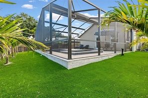 A modern house with a glass enclosure, a pool, and a well-maintained lawn. - Osprey Oasis - 3BR-Pet Friendly home w/ Private Screened Pool & Jacuzzi (Osprey)