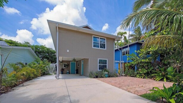 Uma casa de dois andares com garagem coberta, rodeada por vegetação tropical.