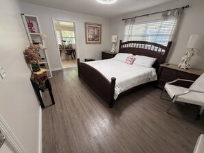 Una camera da letto con un letto in legno, un comodino, una sedia, uno specchio e una porta che dà su un'altra stanza.