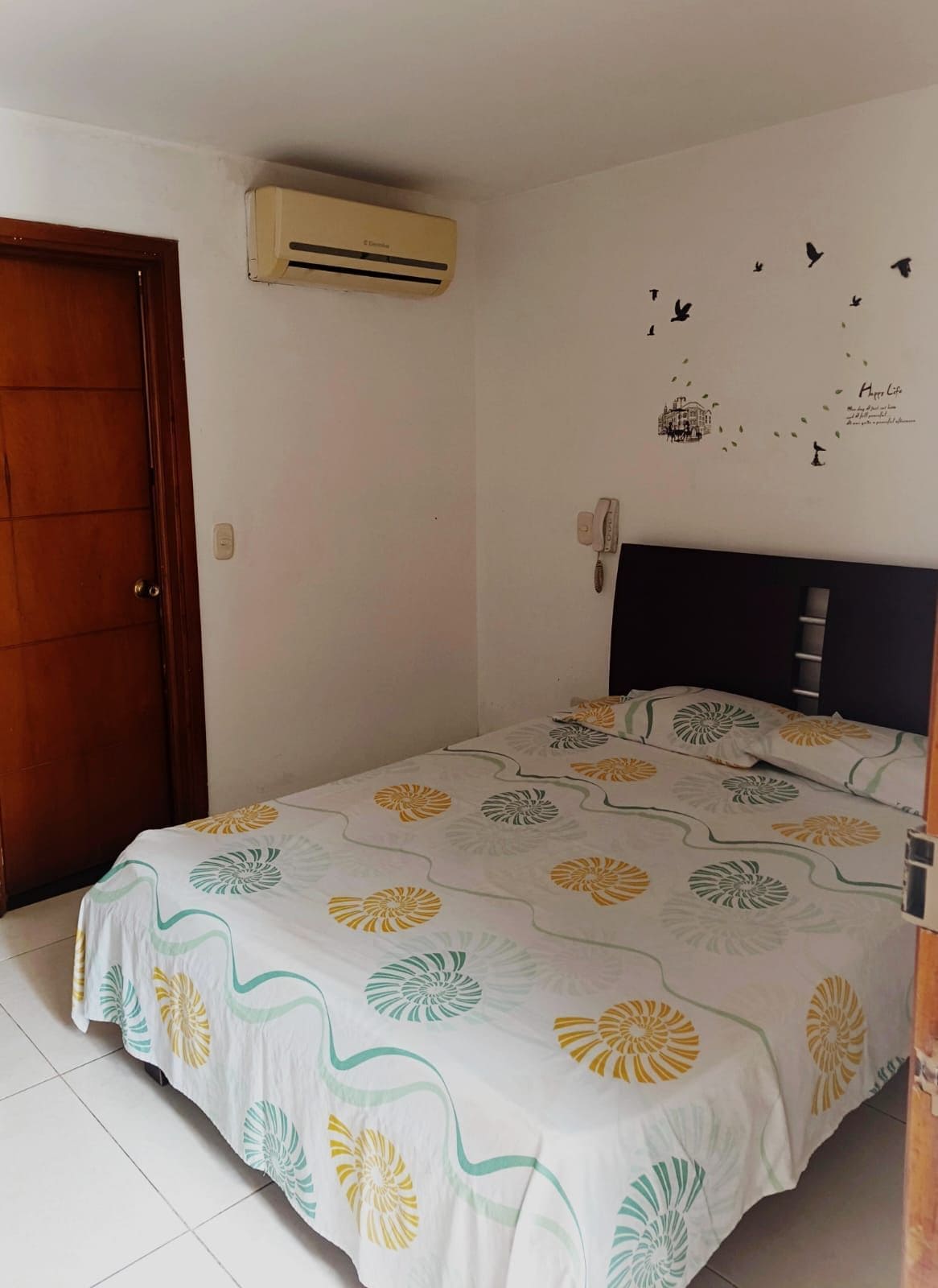 Un dormitorio con cama, aire acondicionado, teléfono en la pared y una puerta.