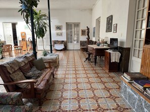 A spacious living room with a patterned floor, a sofa set, a wooden desk, and a television.