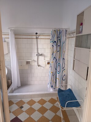 A bathroom with a shower, a toilet, a sink, and a blue bench.