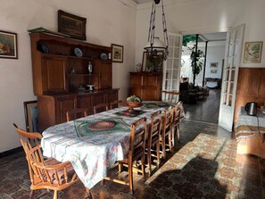 A dining room with a long table, wooden chairs, and a patterned tablecloth.