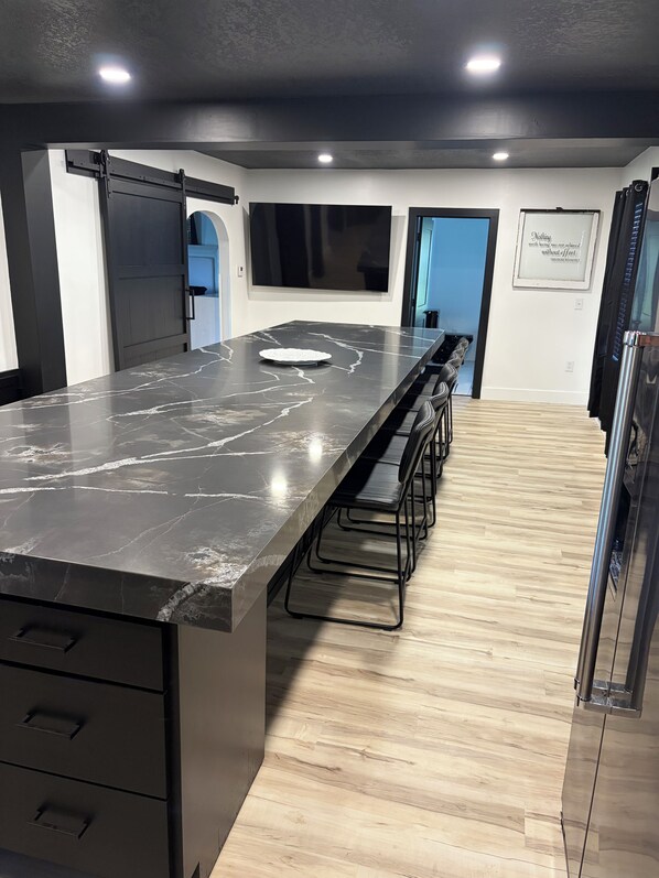 A modern kitchen with a long island counter, black cabinets, and a stainless steel refrigerator.