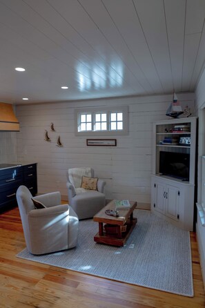 A living room with a sofa, armchair, coffee table, and a television on a cabinet. - Coastal Retreat Between Camden and Rockland (Rockport)