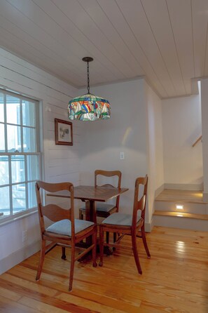 A dining area with a wooden table and chairs, a stained glass pendant light, and a window with a view. - Coastal Retreat Between Camden and Rockland (Rockport)