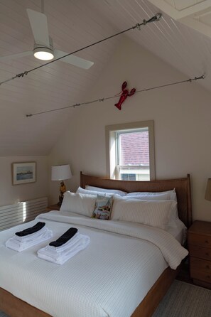 Ein Schlafzimmer mit einem Bett, einem Nachttisch, einer Lampe, einem Deckenventilator und einem Fenster.