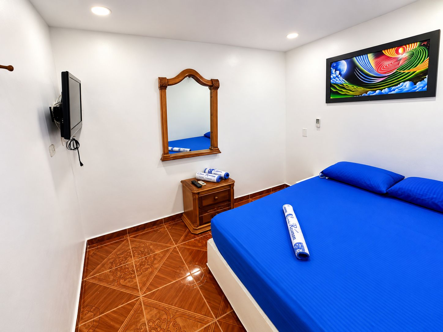 Una habitación de hotel con una cama, un espejo, un televisor y un cuadro en la pared.