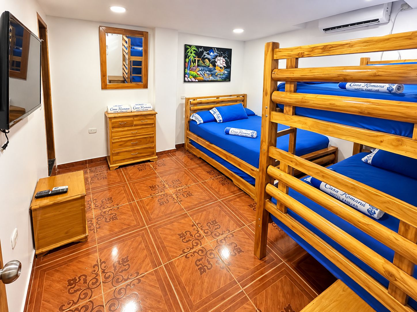 Habitación de hotel con literas, un aparador de madera, un televisor y un cuadro en la pared.