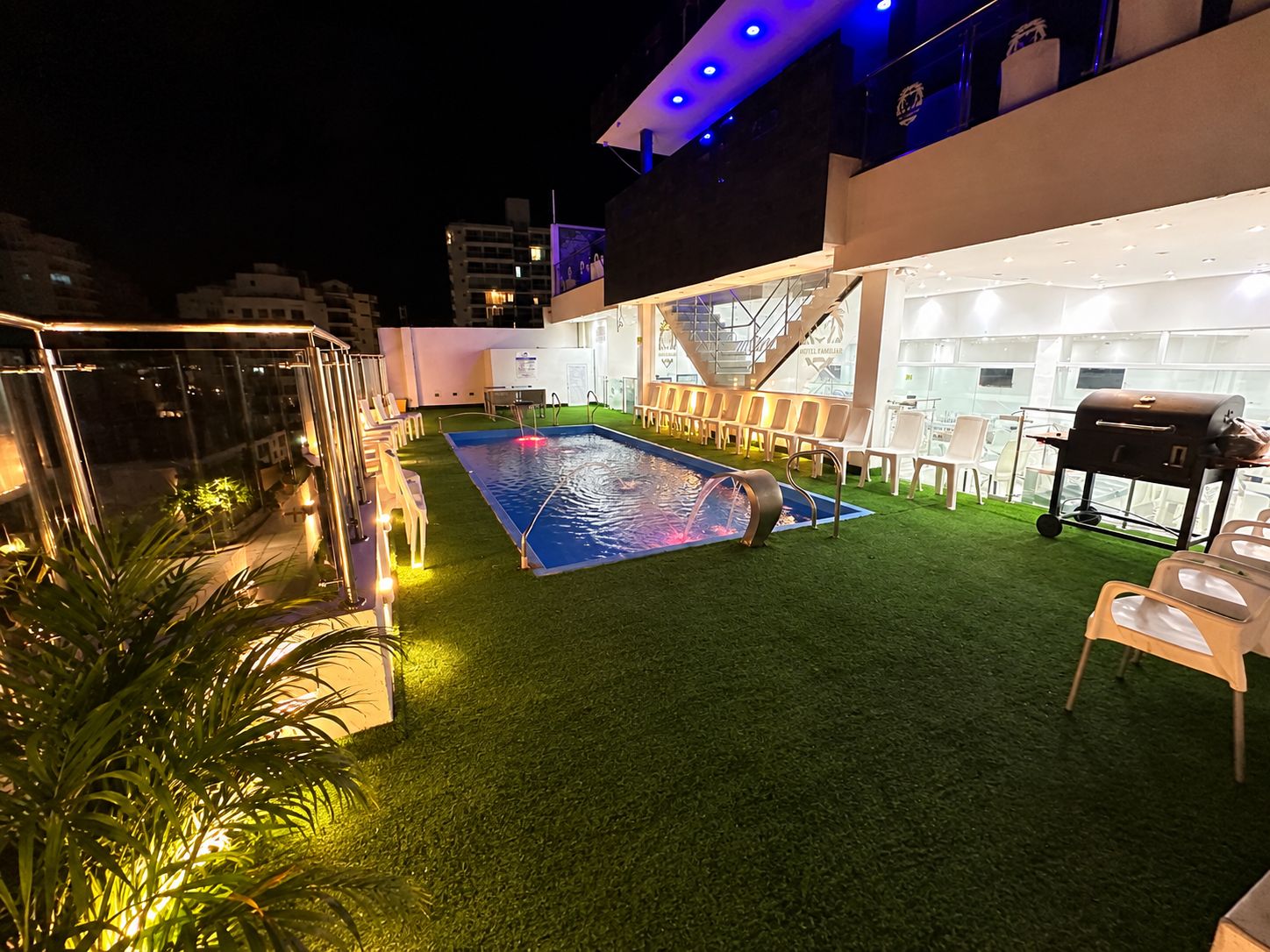 Un área de piscina en la azotea con césped artificial, un elemento decorativo de agua y una zona de barbacoa.