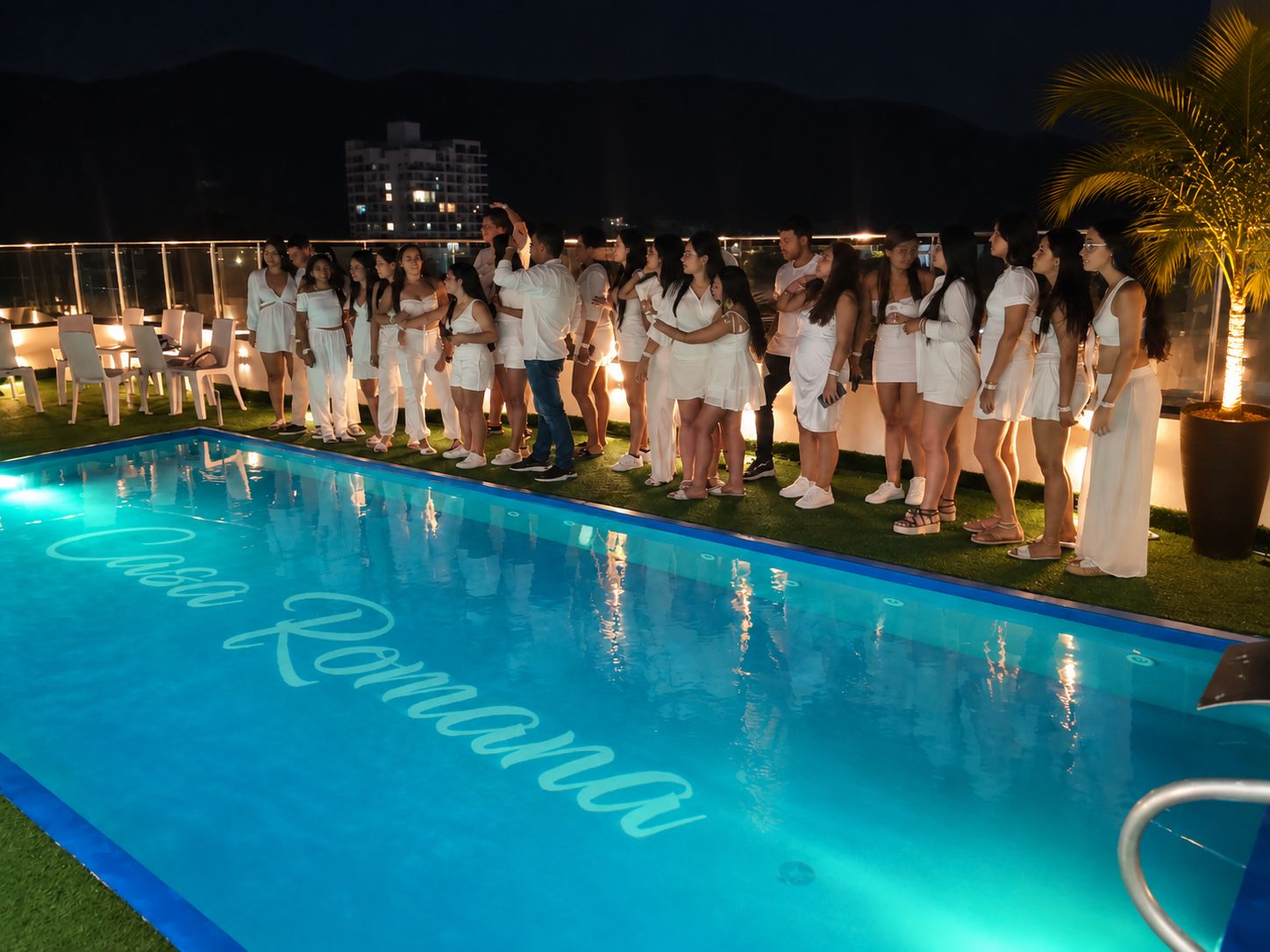 Um grupo de pessoas ao lado de uma piscina, com a inscrição 'Casa Romana' na água.