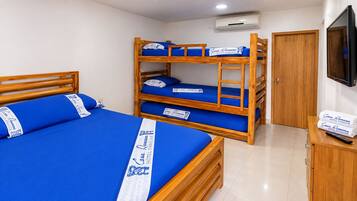 Una habitación de hotel con literas, una cama individual, un armario de madera, un televisor y un aire acondicionado.
