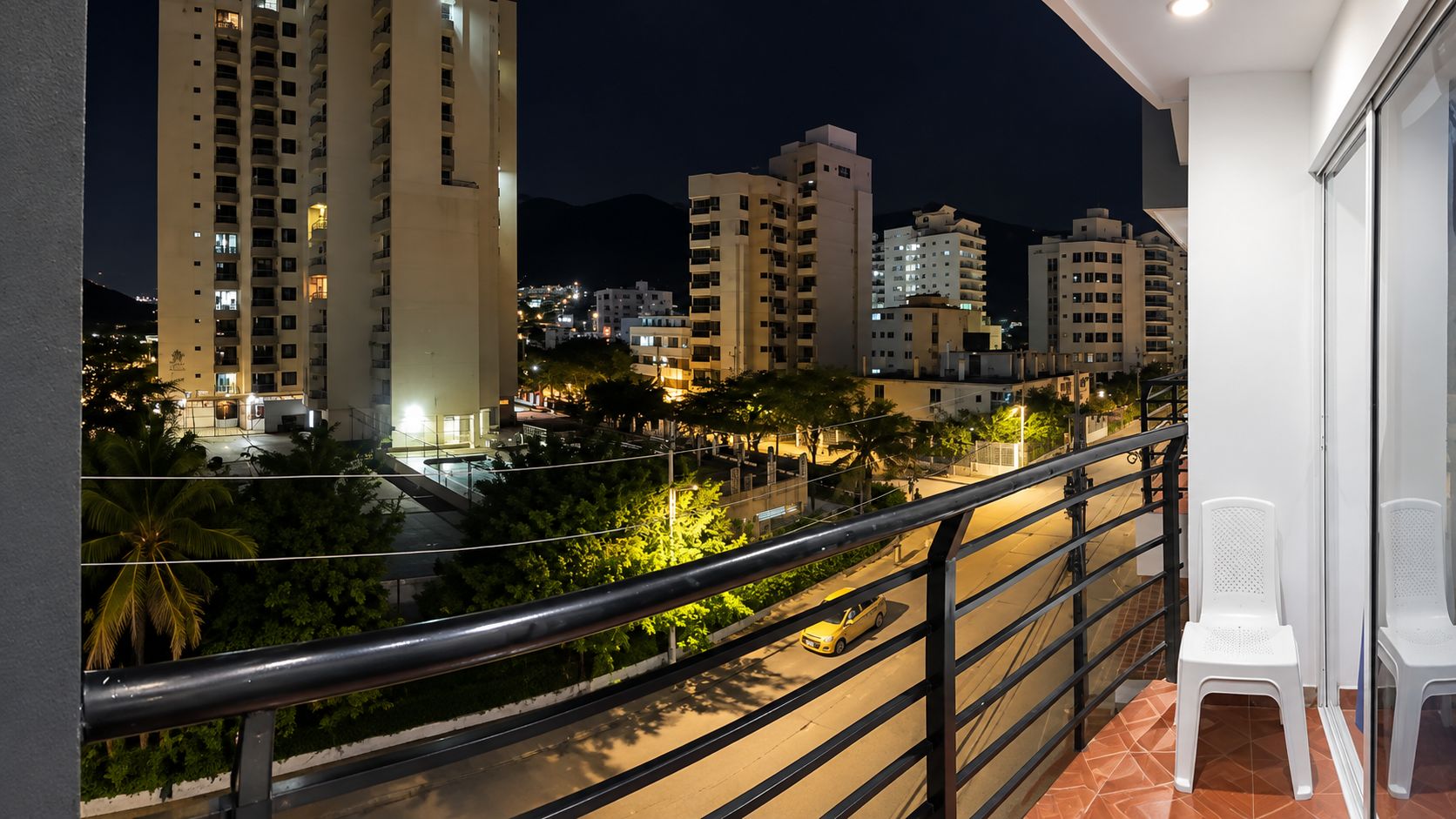 Varanda com guarda-corrimão de metal vista para a cidade à noite.