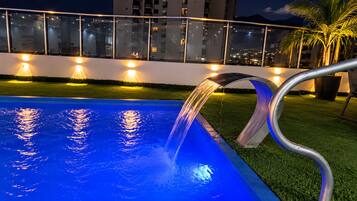 Una piscina con fuente, rodeada por una barandilla de vidrio e iluminada con luces ambientales.