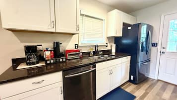 Una cocina con armarios blancos, un refrigerador de acero inoxidable, un lavavajillas y un tostador.