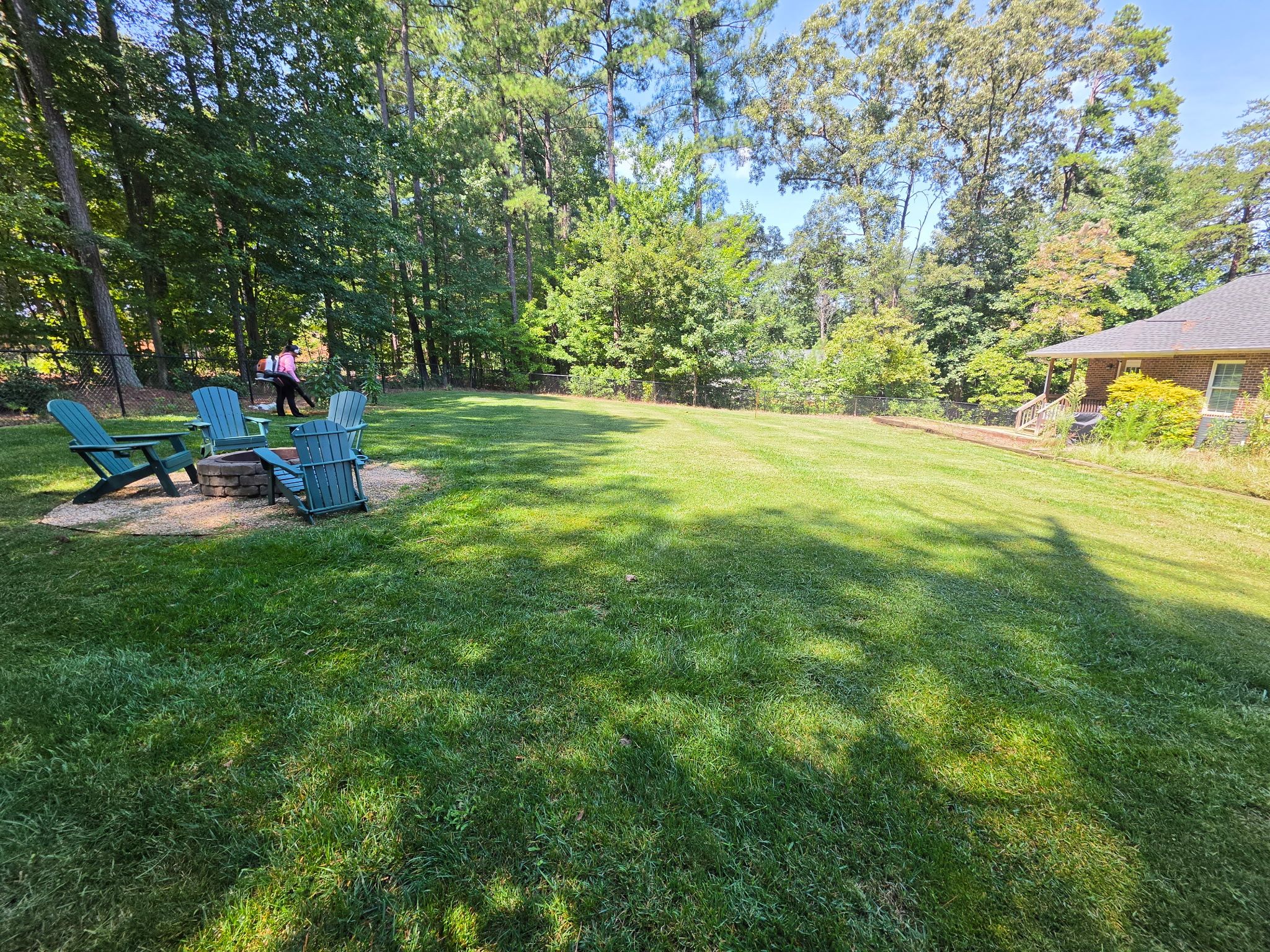 A grassy backyard with a wooden deck, Adirondack chairs, and a small brick building.