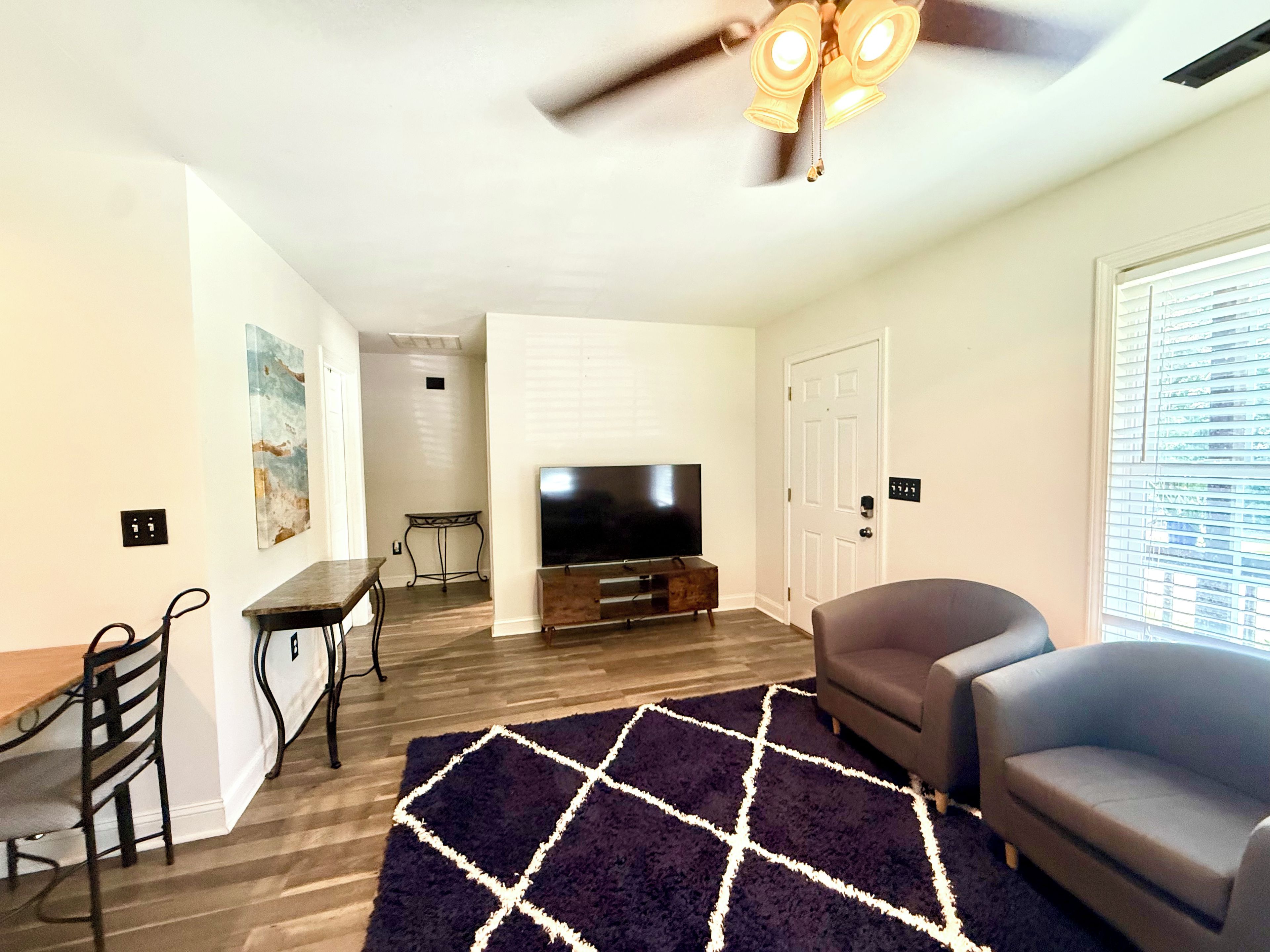 A living room with a flat-screen TV, a ceiling fan, a dining table, and a sofa.