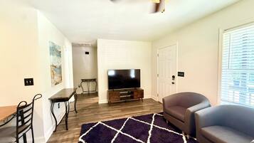 A living room with a flat-screen TV, a ceiling fan, a dining table, and a sofa.