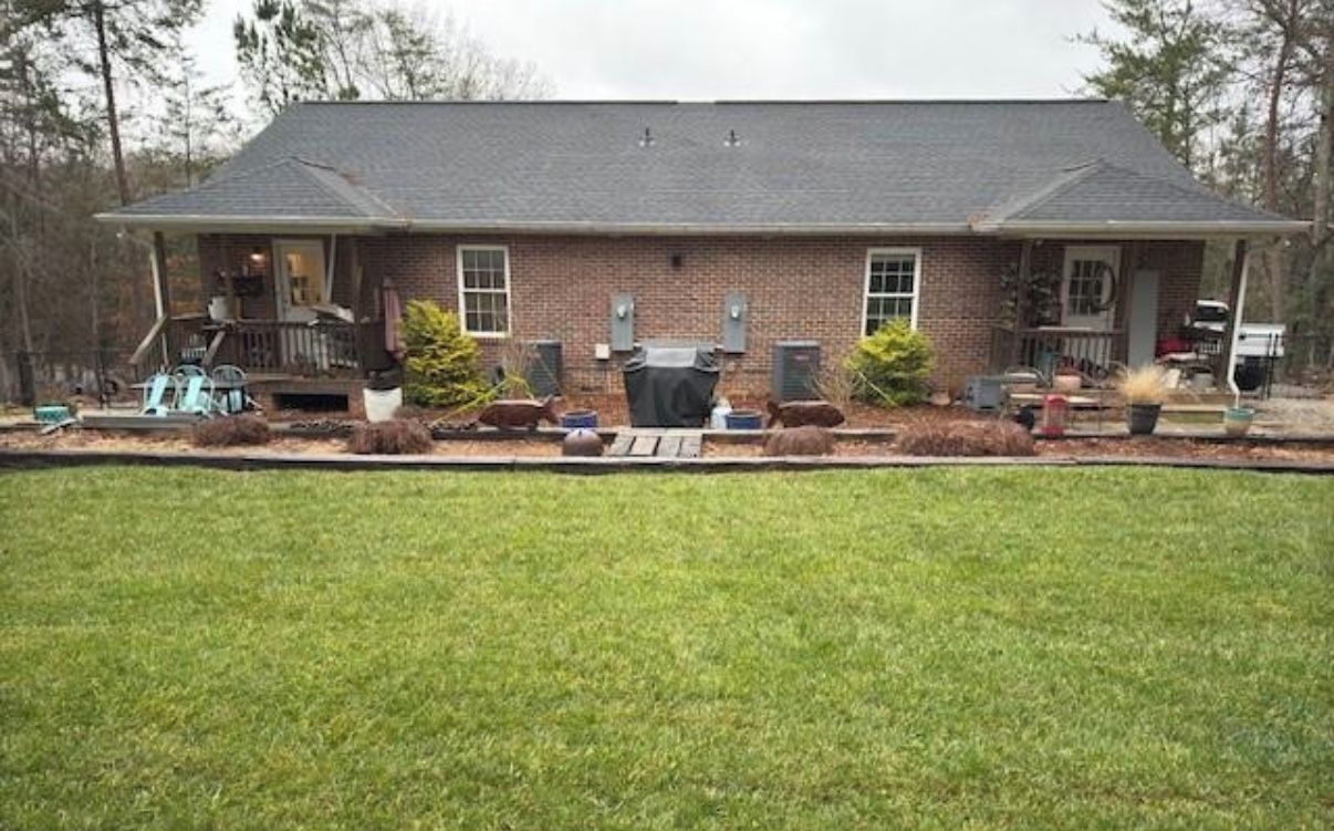 A two-story brick house with a covered porch, a lawn, and outdoor furniture.