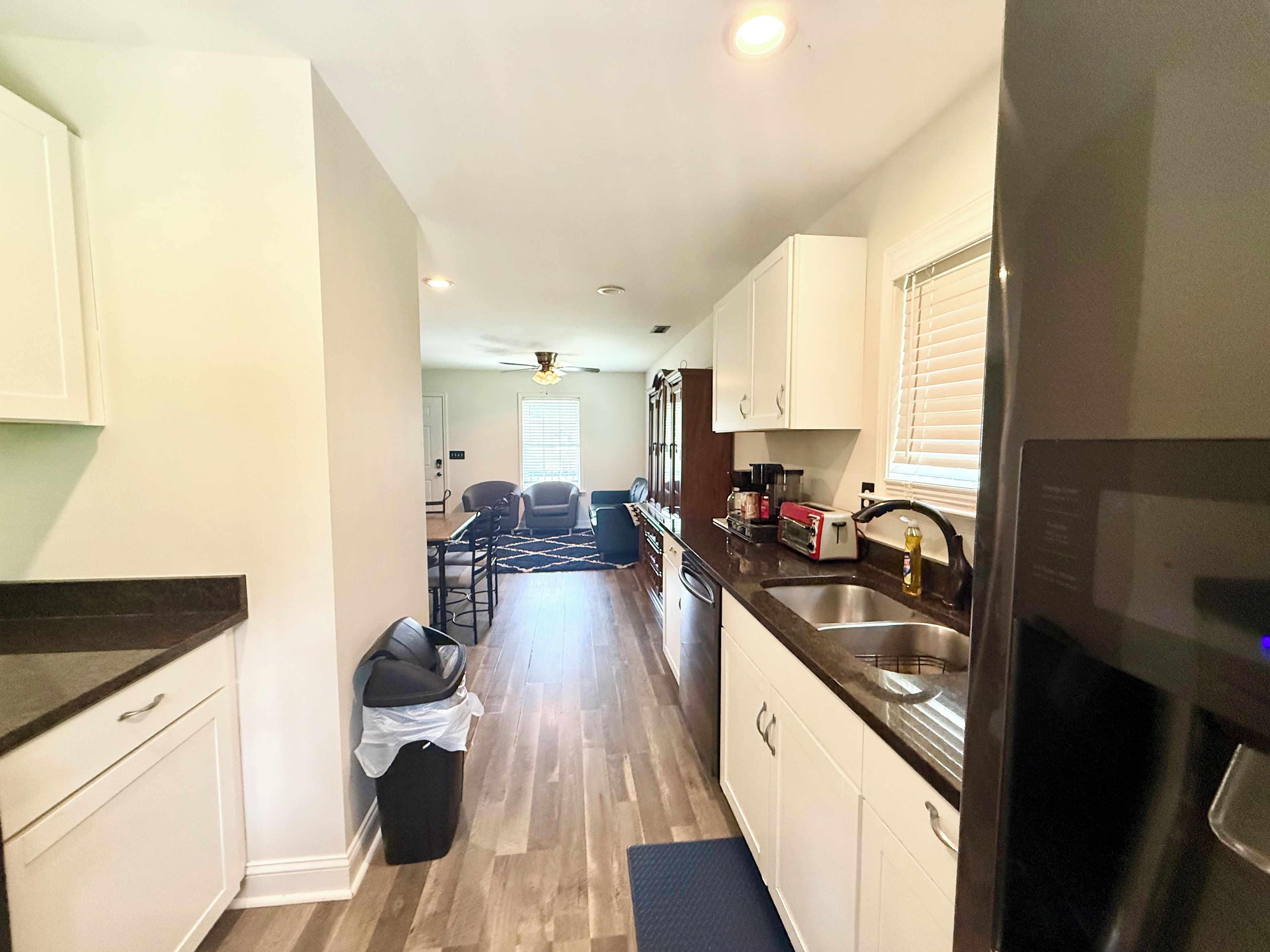 Cocina con microondas, lavamanos y armarios. Hay una zona de comedor con sillas y una mesa.