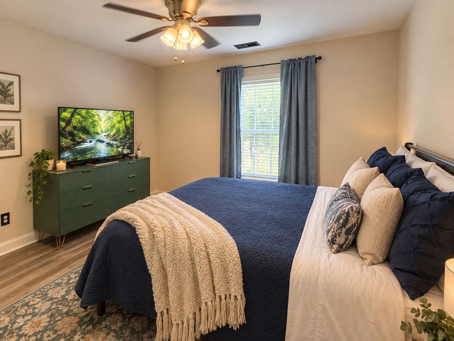 Une chambre à coucher avec un lit, un téléviseur posé sur une commode, un ventilateur de plafond et une fenêtre avec des rideaux.