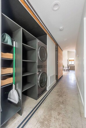 A laundry room with a built-in washer and dryer, a broom, and a mop. - Urban East Austin Retreat (Austin)