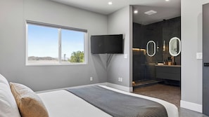 Ein modernes Schlafzimmer mit einem großen Bett, einem flachbildfernseher an der Wand und einem Fenster mit Blick ins Freie.
