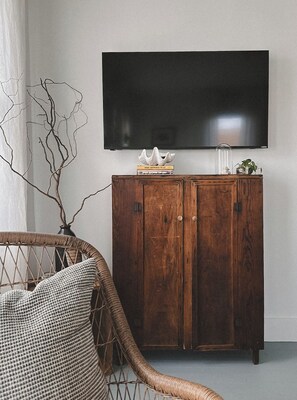 Una habitación con un armario de madera oscura, una silla de mimbre y un televisor de pantalla plana montado en la pared.