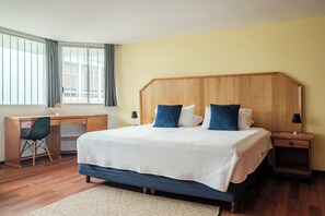Quarto com uma cama grande, uma escrivaninha e uma cadeira.