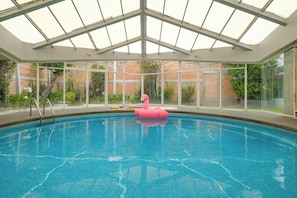 Ein Innenpool mit Glasdach, einem Flamingo-Schwimmding und einer Ziegelwand im Hintergrund.