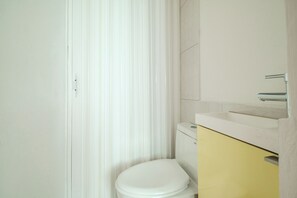 Casa de banho com sanita branca, armário amarelo e lavatório branco.