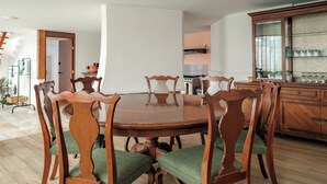Un comedor con mesa y sillas de madera, un armario con puertas de vidrio y una escalera al fondo.