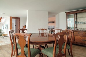 Uma área de refeições com mesa e cadeiras de madeira, um armário com portas de vidro e uma escada ao fundo.