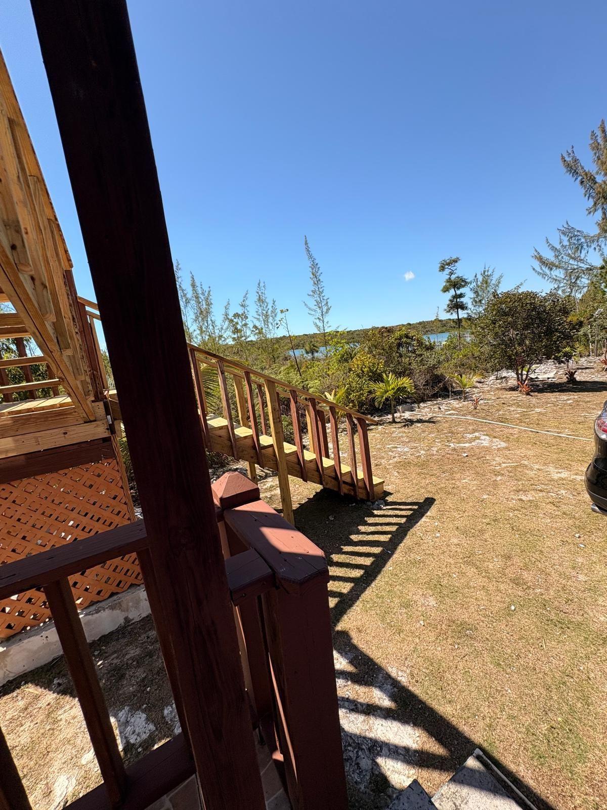 A wooden deck with a staircase leading to a building, surrounded by a dry grassy area with sparse vegetation and a clear sky. - perfect for family. Angler and nature guides (Queens highway)