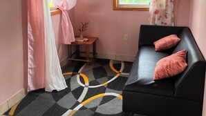 A room with a black sofa, pink cushions, a small wooden table with a vase, a window with curtains, and a flat-screen TV mounted on the wall. - perfect for family. Angler and nature guides (Queens highway)